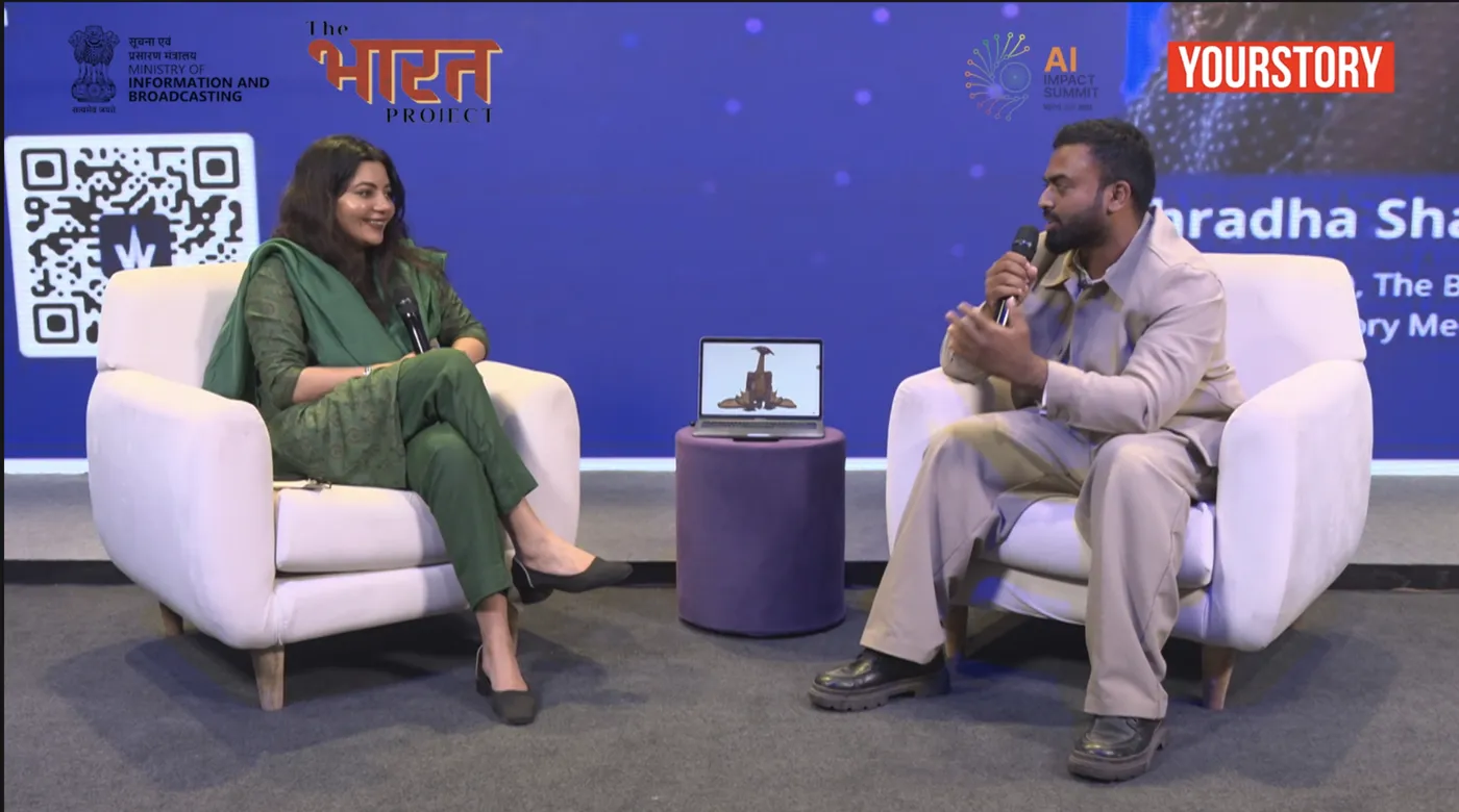 A stage interview at the India AI Impact Summit, with a Character XYZ character shown on a laptop between the two chairs